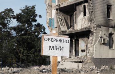 The sign Beware of mines on the background of a destroyed residential building.
