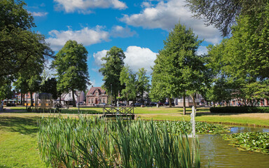 Beautiful idyllic green dutch town park, pond, wood bridge, blue summer sky fluffy clouds - Nuenen,...