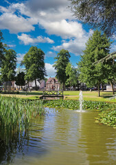 Fototapeta na wymiar Beautiful idyllic green dutch town park, pond, wood bridge, blue summer sky fluffy clouds - Nuenen, Netherlands