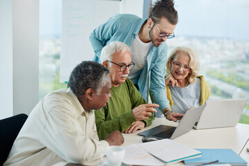 A multiracial group of motivated senior students look at the lesson on a tablet and talk with a...