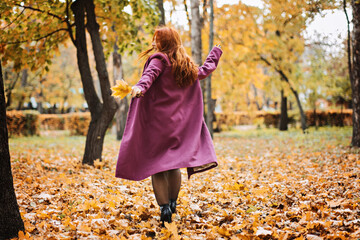 Mental health in autumn. Happy red-haired woman holding yellow maple autumn leaves