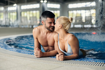 Affectionate couple flirting in the pool at spa center. A happy married couple in love is in the pool with hot thermal and mineral water at the spa center and spending romantic moments.
