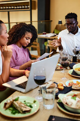 A multicultural busy businesspeople are working on a start-up project in a restaurant at the dinner table.