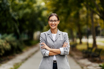 A successful young businesswoman standing in a park with arms crossed. Success will come to you...