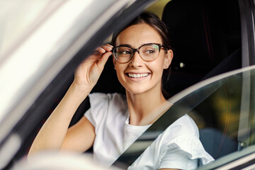 A nerdy girl sitting in her car and looking for a parking spot. A girl in a car