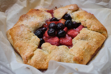 French galette or tart with strawberry and peach on baking paper on culinary background top view. Summer delicious homemade sweet pastries