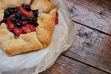 French galette or tart with strawberry and peach on baking paper on culinary background top view. Summer delicious homemade sweet pastries