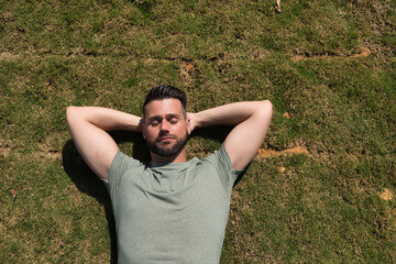 Young and handsome man, with a beard and green shirt, with his eyes closed and his hands behind the...