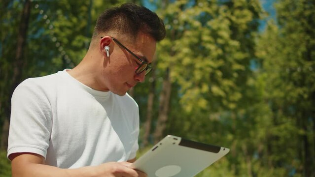Asian man using gadget tablet outdoor close-up. Korean young guy freelancer working remotely in street. Remote work, business. Student communicating with family and friends online, chatting.