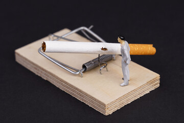 Cigarettes are placed in a mousetrap, next to it is a figure of a man.