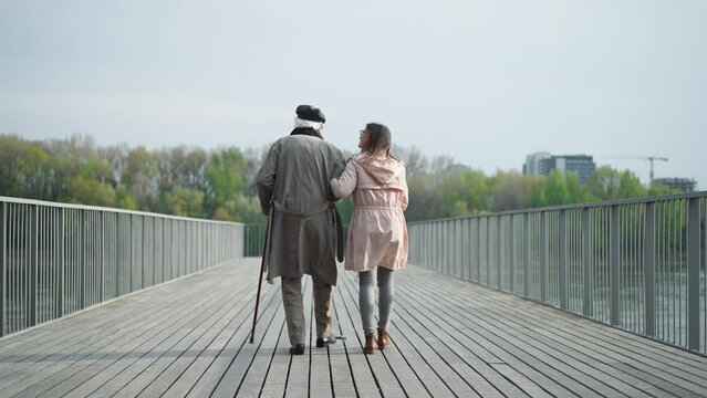 Rear view of senior man with daughter outdoors on a walk on pier by river.