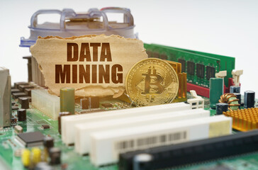 On the motherboard lies a bitcoin coin and a cardboard sign with the inscription - Data mining
