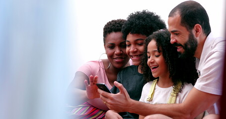 Interracial parents and ethnically diverse kids laughing at social media content on cellphone