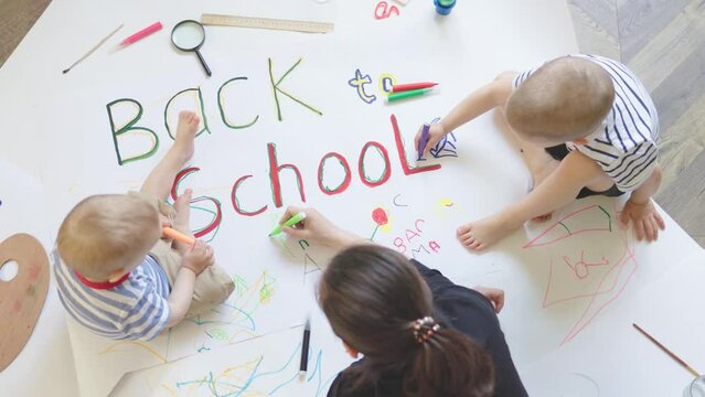back to school concept female woman two little kids children drawing on floor wallpaper phrase words. education kindergarten primary school. colorful pencils. boys brothers sitting indoor room home.