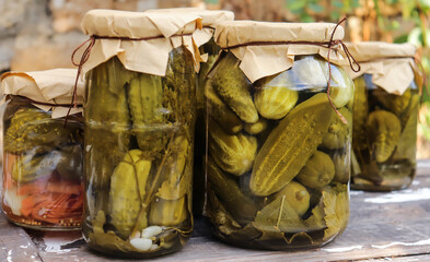 pickled cucumbers in glass jars close-up on a wooden table against the background of a stone wall selective focus
