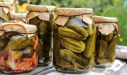 pickled cucumbers in glass jars close-up on a wooden table against the background of a stone wall...