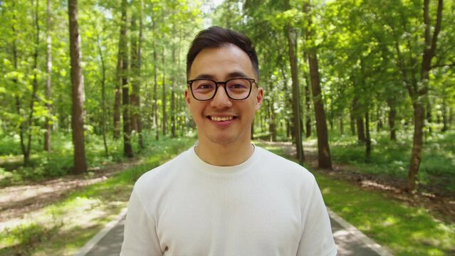 Happy Asian man portrait outdoor. Young Korean guy walking in park, cheerful male person looking in camera, smiling and posing. Summer sunny day.