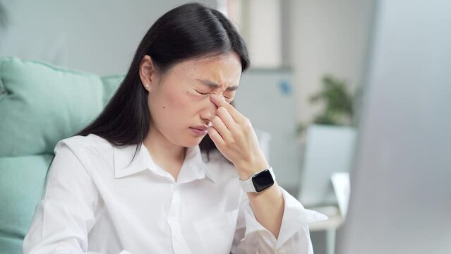 Exhausted, overworked asian office worker sitting in the workplace with severe headache massaging his head. unhealthy Tired female employee in pain ache sick Stress sedentary working computer. Asia