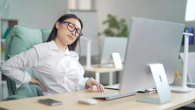 Young Asian Woman Affected Back Ache At The Workplace. Female Backpain Sitting For A Long Time At The Computer Desk In The Office. Indoor. An Employee Entrepreneur Suffers From Pain Tension. 