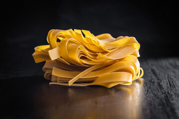 Uncooked pappardelle pasta on black table.