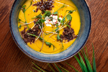 Vegetarian autumn creamy pumpkin soup with herbs on wood background