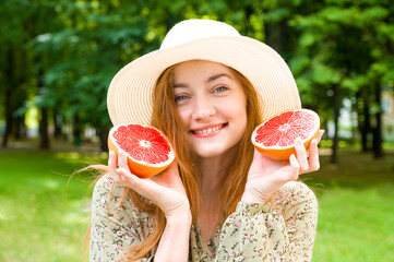 Young happy red haired female in a hat holding grapefruit. Summer portrait concept. Fruit and...