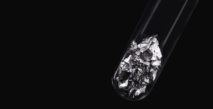 Chromium fragments inside test tube, industrial use ore, metallic chemical element, isolated on black background