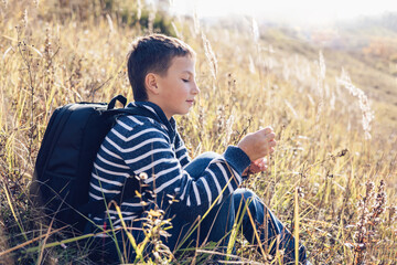 Autumn portrait of teenager boy sitting on grass. Young man with backpack resting relaxing,...