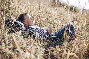 Autumn portrait of teenager boy with backpack lying on grass. Happy child with backpack resting...