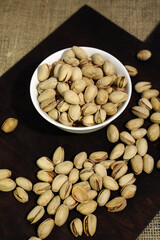 Useful roasted pistachios in a ceramic bowl on a dark wooden background.