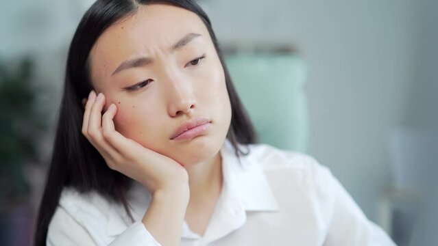 Bored sleepy Asian office worker sitting at work workplace at computer desk leaning on hand. Tired woman. Exhausted young Businesswoman employee. Portrait Depressed, unhappy, workless female manager