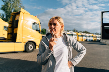 Caucasian mature woman in middle age working as a truck driver. Smoking on a parking lot of trucks