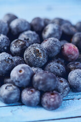 fresh raw blueberries on blue background with water drops, vertical color photo