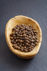 Allspice in wooden bowl on dark slate background with copy space