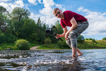 The photographer is knee-deep in the water and takes off the flow of water. A videographer shoots a waterfall. Photographer in the wild.