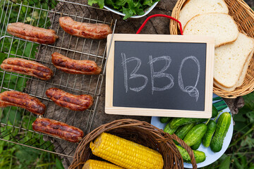 Barbecue inscription on chalkboard, grilled sausages, corn,bread. Outdoor recreation concept.