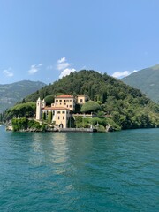 Fototapeta na wymiar Landscape of Como Lake shore and Villa del Balbianello mansion house surrounded by trees. Emerald blue water. Tremezzo, Como Lake, Lombardy, Italy