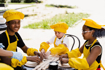 Multiethnic cooks children in yellow chefs hat and apron cooking dough for bakery. Black african...