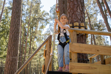 Happy little girl enjoying activity in a climbing adventure park on a sunny day