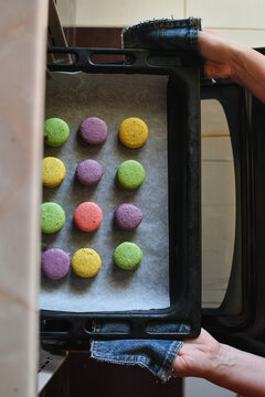 Woman hands taking tray with multicolored macaroons pastry out from the oven. Selective focus. 