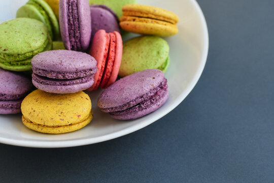 Detail of multicolored macaroons in white ceramic bowl on grey background. Close up, selective focus.  