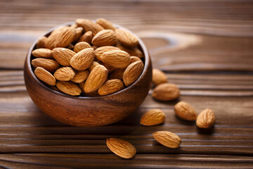Delicious almonds in wooden bowl on wooden background