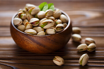 Delicious pistachios in wooden bowl on wooden background