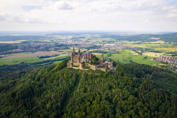 Fototapeta na wymiar Drone shot of Hohenzollern Castle on forested mountain top in the Swabian Alps in summer. Scenic aerial view of old German Burg. Famous fairytale Gothic landmark in Stuttgart vicinity