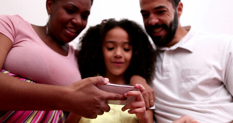 Fototapeta premium Mixed race couple and child holding smartphone. Father pointing to screen laughing and smiling