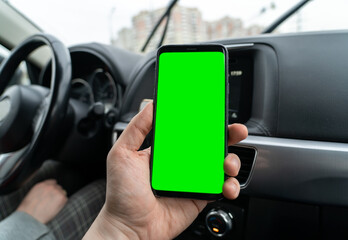 Mobile phone with green screen in hand of man inside car. Smartphone with searching address and pin location via map navigator application, direction of travel, address search, message, location