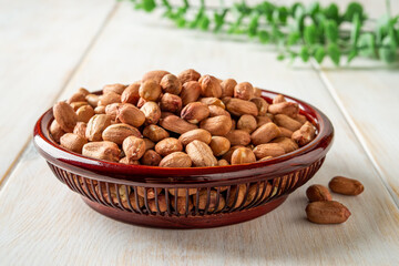 Dried peanut in a wooden bowl over white rustic table. Healhy vegetarian snack of whole peeled monkey nut. Raw groundnut seeds for ready to eat dietary nutrition. Arachis hypogaea fruits.
