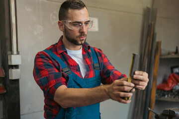 Young male mechanic being focused on measuring out elements for machine at his work space