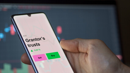 An investor's analizing the grantor’s trusts etf fund on a screen. A phone shows the prices of Grantor’s trusts