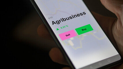 An investor's analizing the agribusiness etf fund on a screen. A phone shows the prices of Agribusiness